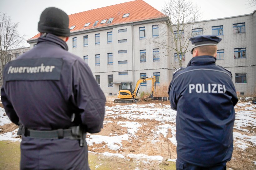 Feuerwerker und Polizist beobachten wie ein Bagger Erdschichten über der Bombe abträgt